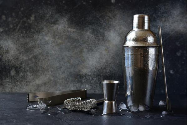 A shaker and bartools on a table against a grey background